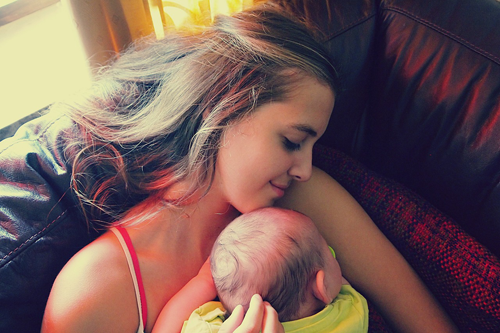 Imagen de una madre descansando en el sofá sosteniendo a su bebé contra su pecho